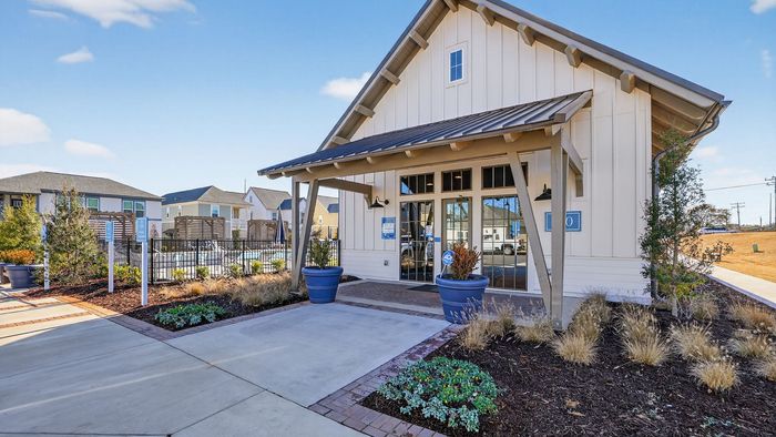 Charming clubhouse entrance with modern design, lush landscaping, and bright blue planters, perfect for welcoming residents.