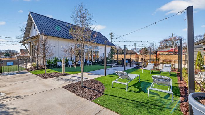 Charming outdoor patio area featuring sleek lounge chairs, lush greenery, and string lights, perfect for relaxation and leisure.