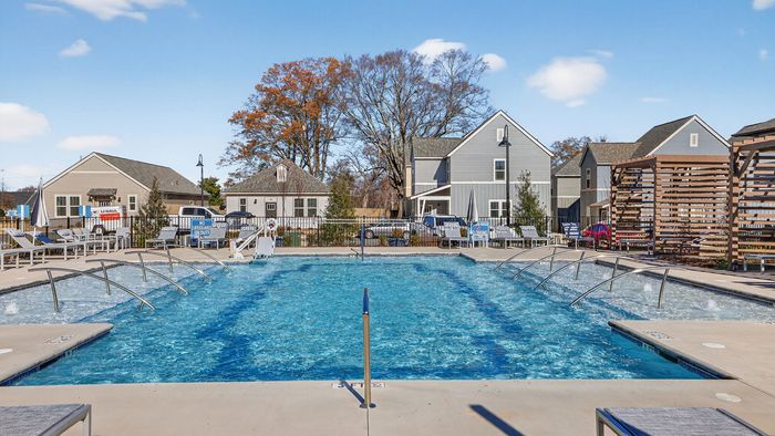 Luxurious outdoor swimming pool area with modern sun loungers and charming homes in the background, perfect for relaxation and enjoyment.