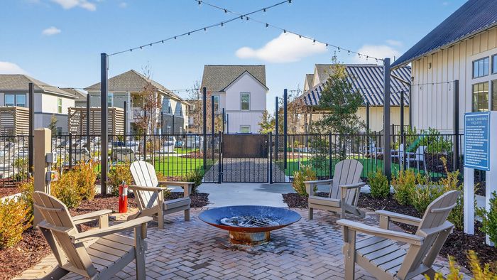 Charming outdoor patio with cozy fire pit, stylish Adirondack chairs, and vibrant landscaping in a modern townhouse community.