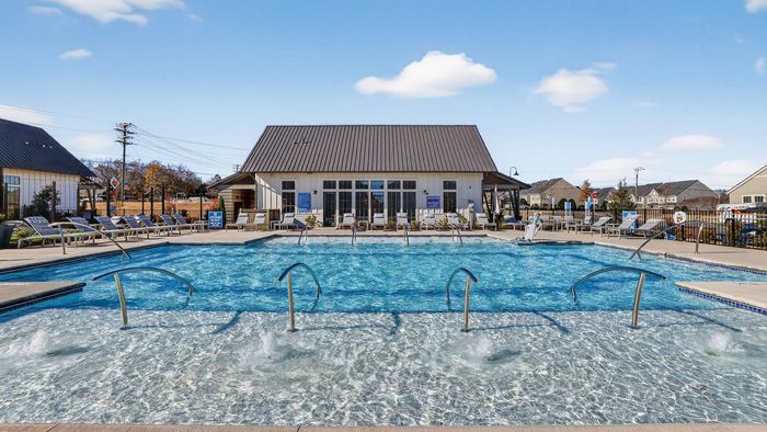 Luxurious outdoor pool area with sparkling water, surrounded by chic lounge chairs and a stylish clubhouse under a clear blue sky.