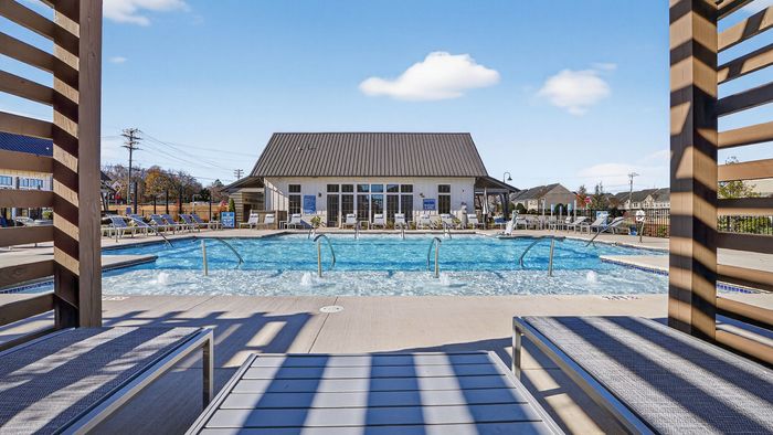 Inviting outdoor pool area with lounge chairs, modern clubhouse, and clear blue skies, perfect for relaxation and entertainment.