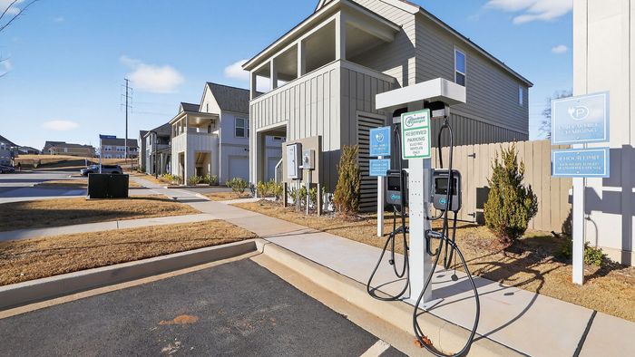 Modern apartment complex with eco-friendly electric vehicle charging stations, surrounded by pristine landscaping and well-maintained walkways under a clear blue sky.