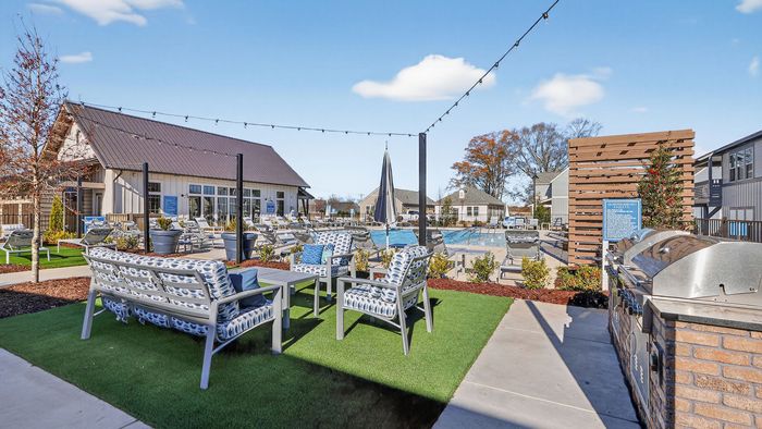 Vibrant outdoor community area featuring cozy seating, modern barbecue grills, and a sparkling pool set against a clear blue sky.