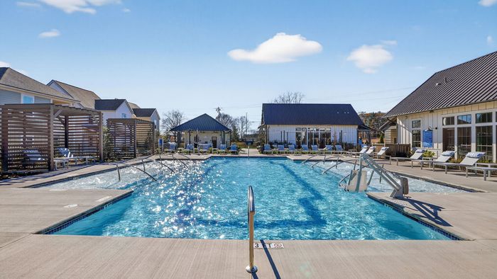 Inviting residential community pool surrounded by stylish lounge chairs and modern cabanas under a clear blue sky.