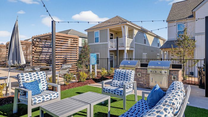 Charming outdoor seating area featuring modern chairs and tables, surrounded by lush greenery and vibrant homes, perfect for a relaxing retreat.