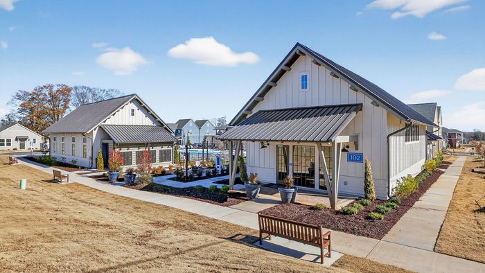 Charming community clubhouse with modern farmhouse design, beautifully landscaped gardens, and inviting pathways under a clear blue sky.