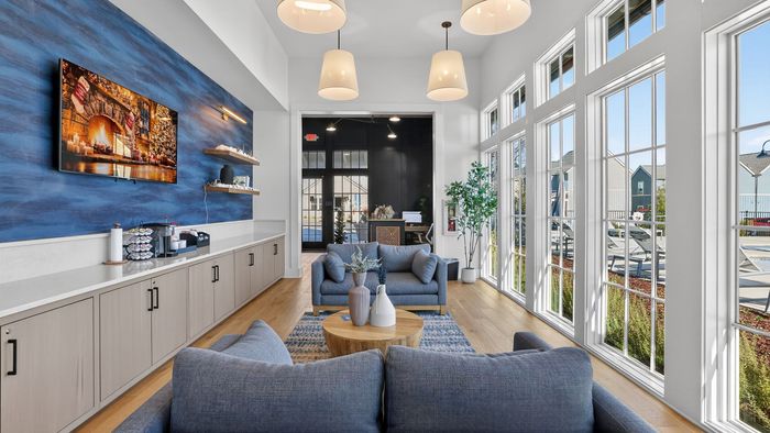 Bright modern living area with large windows, cozy blue sofas, and stylish decor, ideal for relaxation and entertainment.