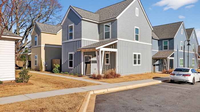 Charming, modern townhome with elegant gray and beige siding, set in a quiet, sunlit neighborhood featuring landscaped lawns and convenient parking.