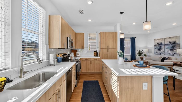 Bright, modern open-plan kitchen with sleek wood cabinets, stainless steel appliances, and a large dining island seamlessly flowing into a cozy living area.