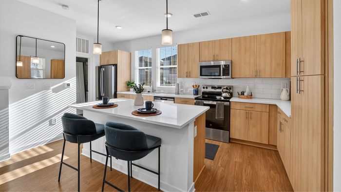 Modern kitchen with sleek white countertops, elegant wood cabinetry, and stainless steel appliances, bathed in natural light.