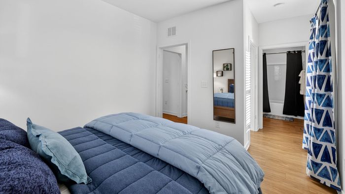 Inviting bedroom with a cozy blue-themed decor, featuring a plush bed, elegant hardwood flooring, and a modern en-suite bathroom.