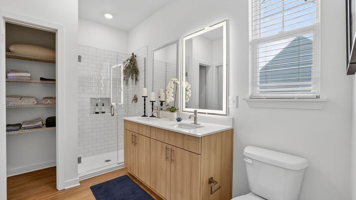 Elegant bathroom featuring a modern double vanity, large illuminated mirror, and chic glass shower, enhanced by natural light and warm wood flooring.