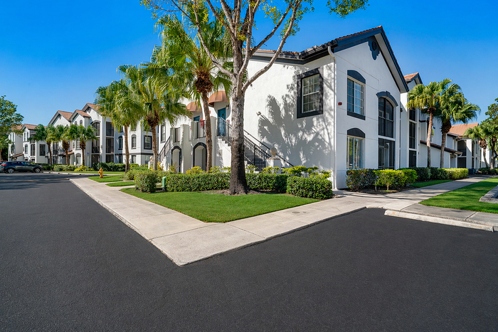 Charming apartment complex with elegant architecture, lush palm trees, and manicured landscaping under a clear blue sky.