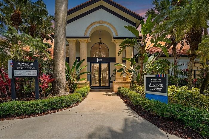 Elegant leasing office entrance with Mediterranean-style architecture and lush tropical landscaping, inviting residents to Advenir Living.