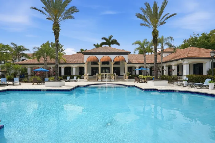 Luxurious apartment complex with a stunning poolside view, palm trees, elegant architecture, and inviting sun loungers.