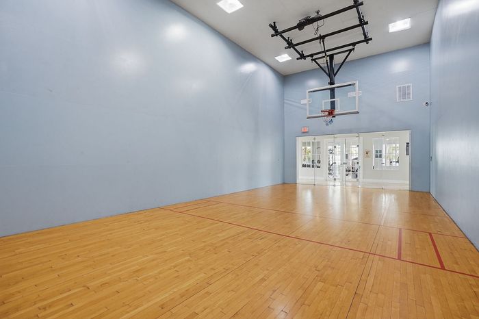 Modern indoor basketball court with polished wooden floors, high ceiling, and mounted hoop, perfect for sports enthusiasts.
