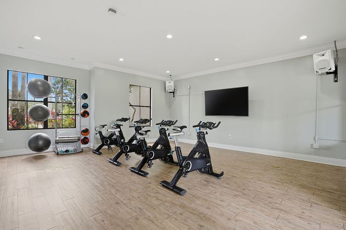 Modern fitness room with exercise bikes, yoga balls, and a wall-mounted TV, perfect for a lively workout session.