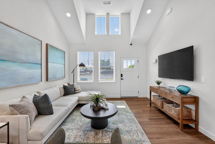 Bright, contemporary living room featuring high ceilings, elegant decor, a spacious sectional sofa, and natural light through large windows.