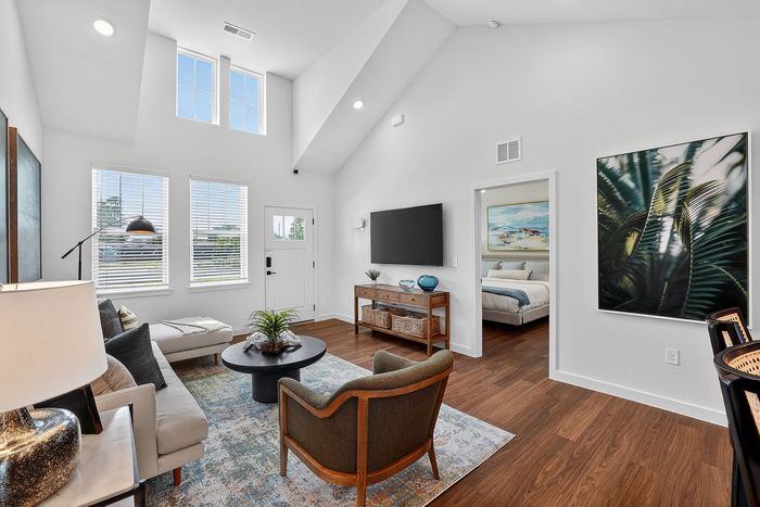 Bright and airy living room with vaulted ceilings, stylish decor, and natural light, leading to a cozy bedroom.