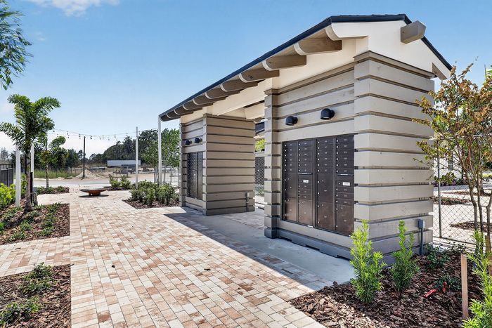 Chic outdoor parcel locker area with modern mailbox units, lush landscaping, and ambient string lights under a clear blue sky.