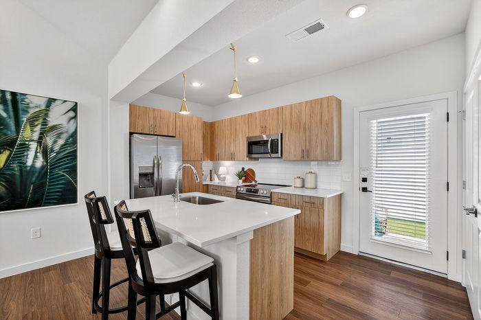 Modern kitchen with light wood cabinetry, sleek white countertops, and elegant pendant lighting, featuring a stainless steel fridge and a cozy breakfast bar.