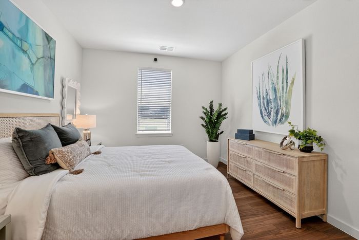 Inviting bedroom with elegant decor, featuring a cozy bed, large artwork, and a wooden dresser, all bathed in natural light.
