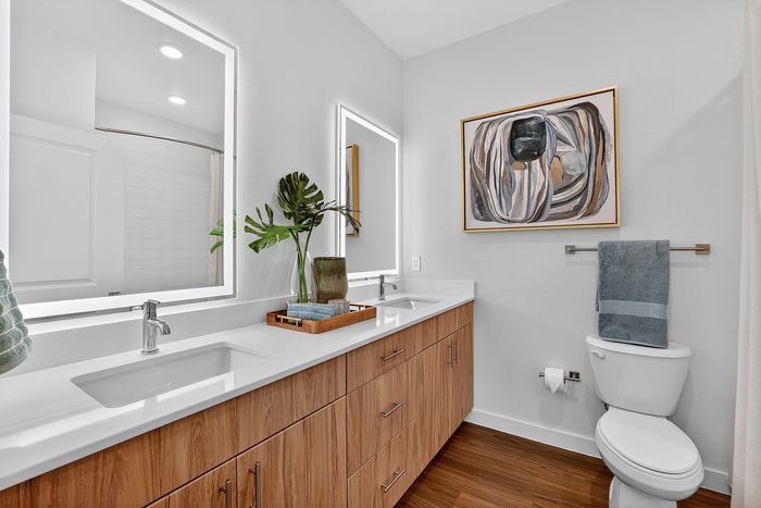 Modern bathroom with sleek wooden cabinetry, dual sinks, stylish wall art, and elegant lighting.