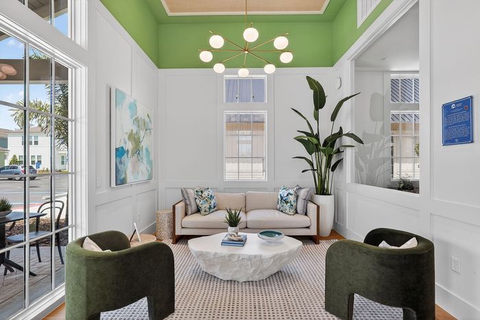Bright and modern living room with a chic white sofa, vibrant green chairs, and elegant decor, featuring large windows and lush plant accents.