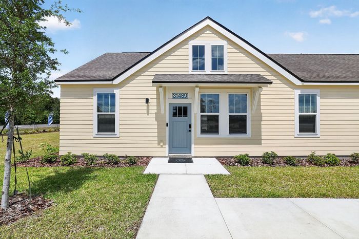 Charming single-story yellow house with a welcoming blue door, surrounded by a lush green lawn and landscaped garden, under a clear blue sky.