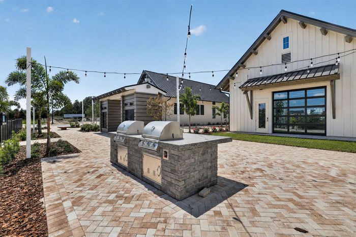 Charming outdoor patio with modern brick grills and cozy string lighting, perfect for entertaining, surrounded by lush landscaping and a stylish building facade.