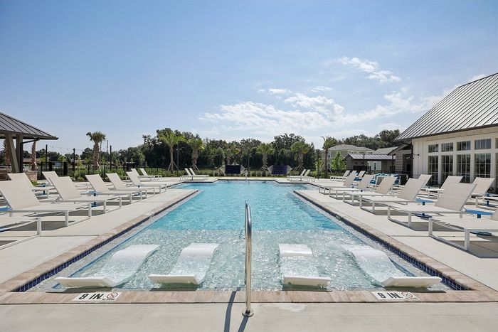 Inviting outdoor pool area featuring luxury loungers and shaded cabanas, surrounded by lush greenery and clear skies.