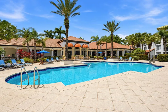 Inviting resort-style pool with elegant lounge chairs and lush palm landscaping at a luxury apartment complex.