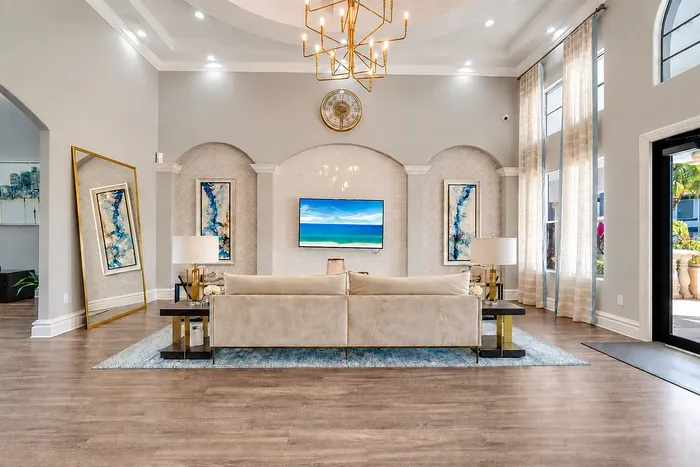 Luxurious living room with high ceilings, elegant chandelier, and contemporary decor, featuring a plush beige sofa and a modern wall-mounted TV.