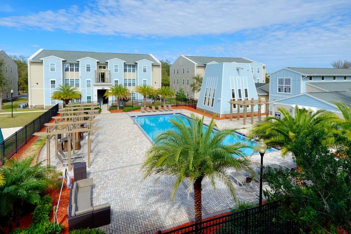 Top view of the sparking pool and pergolas | Outdoor sofas and lounge chairs provide seating | Apartment buildings surround the pool area | Hawks Landing