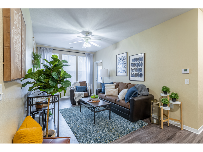 Interior view of the living room | Ample natural lighting accompanies a ceiling fan light fixture | entertainment center set in front of sofa and coffee table | Hawks Landing Apartments in Tampa, FL
