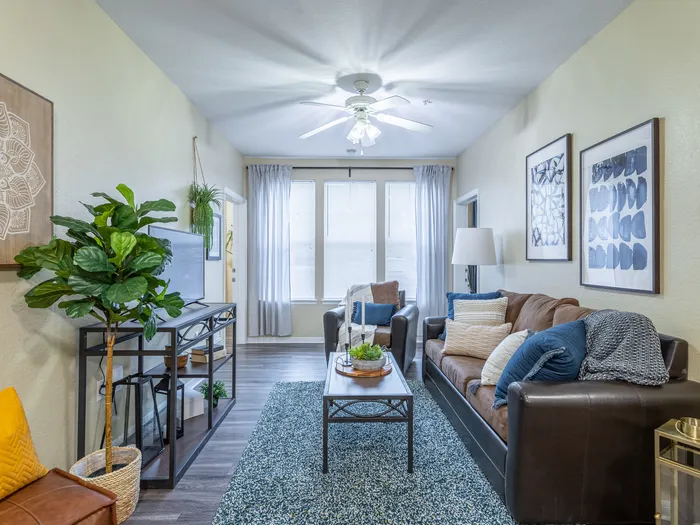 Interior view of the living room | Ample natural lighting accompanies a ceiling fan light fixture | entertainment center set in front of sofa and coffee table | Hawks Landing Apartments in Tampa, FL