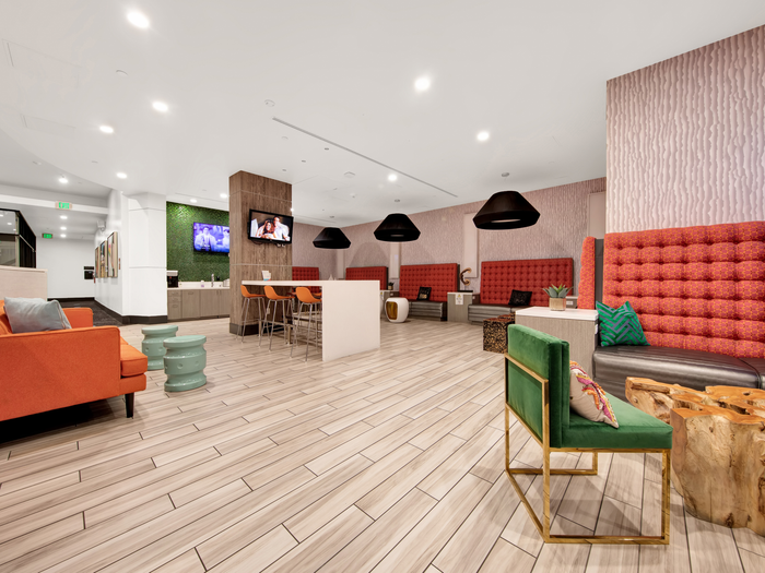 Clubhouse with plank-style flooring and suspended lights orange panels and seating in common area | University Gateway Apartments in Los Angeles, CA.