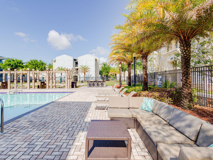 Seating and chaise lounges on sun deck with palm trees in background and pool  | Hawks Landing | Apartments in Tampa, FL