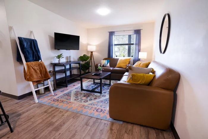 Living room with couch, chair, mounted TV, and coffee table in apartment at Tech Village, student  housing.