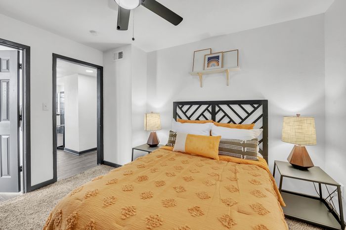 Modern bedroom with a stylish bed featuring orange bedding, side tables, and warm lighting.
