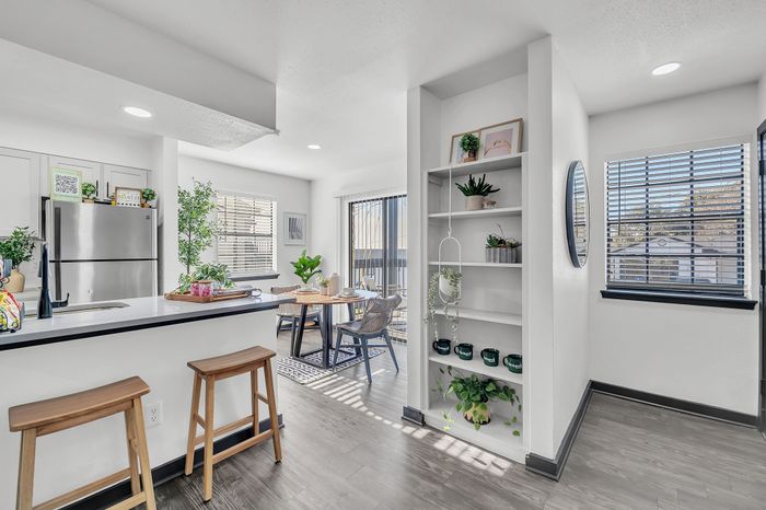 Bright and modern kitchen with bar stools, stainless steel appliances, and adjacent dining area with greenery.