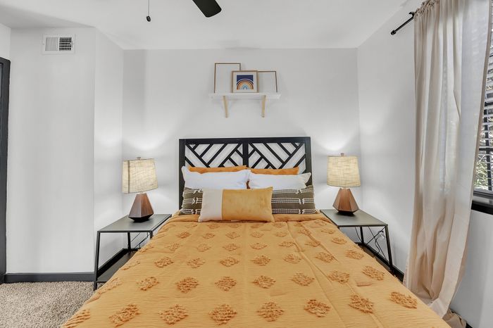 Inviting bedroom with a stylish bed adorned with a vibrant orange cover, modern side lamps, and decorative art.