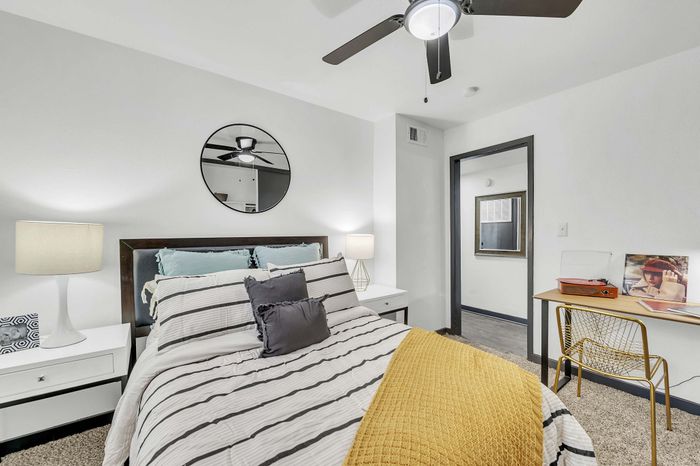 Stylish bedroom with a striped bedspread, circular mirror, and cozy workspace in a modern apartment.