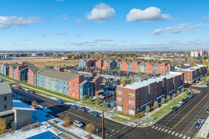 Vibrant aerial view of colorful apartment buildings in a picturesque suburban setting, framed by clear blue skies and scenic landscapes.