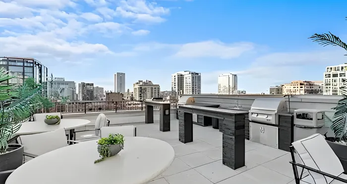 Luxurious urban rooftop terrace with modern dining set, skyline views, and built-in barbecue station.
