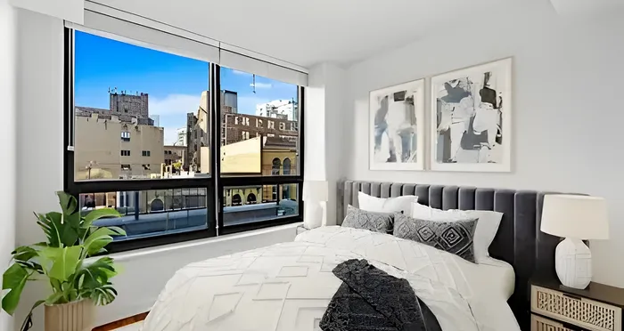 Modern bedroom with plush bed, large windows showcasing a vibrant cityscape, and stylish artwork enhancing the contemporary decor.