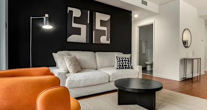 Contemporary living room featuring a chic black accent wall, cozy white sofa, vibrant orange chairs, and modern artwork.