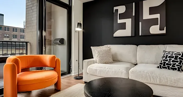 Chic and modern living room with a striking orange chair and cozy cream sofa, complemented by contemporary black-and-white artwork. Urban views add a stylish vibe.