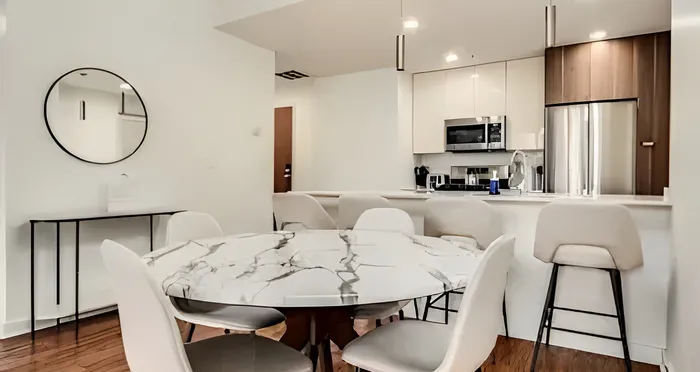 Elegant dining area with a marble table and chic seating, adjacent to a modern kitchen featuring stainless steel appliances and sleek cabinetry.